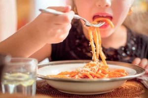 A child eating a bowl of cooked pasta with red sauce.