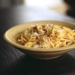 A bowl filled with spaghetti carbonara, topped with freshly grated Parmesan.