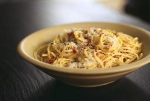 A bowl filled with spaghetti carbonara, topped with freshly grated Parmesan.