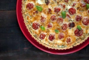 A cooked cherry tomato tart with a herbed crust on a red plate.
