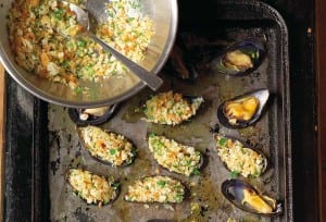 A rimmed baking sheet with stuffed broiled mussels and a bowl of filling on the side