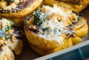 A casserole dish with four halves of roasted winter squash filled with cheese-topped stuffing
