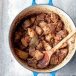 Blue pot of chunks of pork, authentic carnitas, with a bay leaf and wooden spoon on top