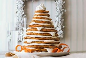A stack of carrot cake pancakes layered with mascarpone frosting, shaped to look like a Christmas tree on a white plate.