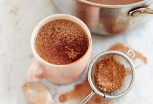 A pot and a mug filled with paleo hot cocoa and a sifter of cocoa powder on the side