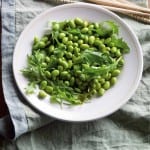 A white bowl filled with edamame salad sitting on a grey linen napkin with chopsticks on the side