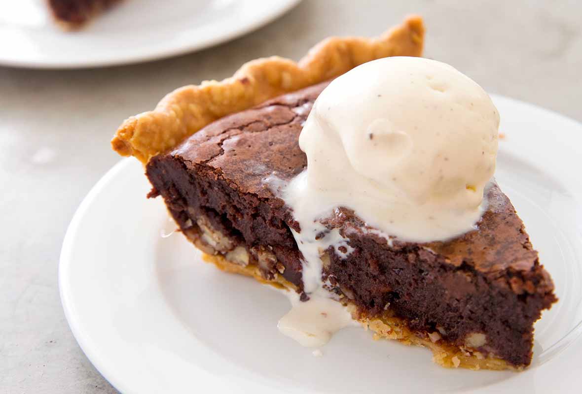 A slice of brownie tar heel pie on a white plate topped with a scoop of vanilla ice cream