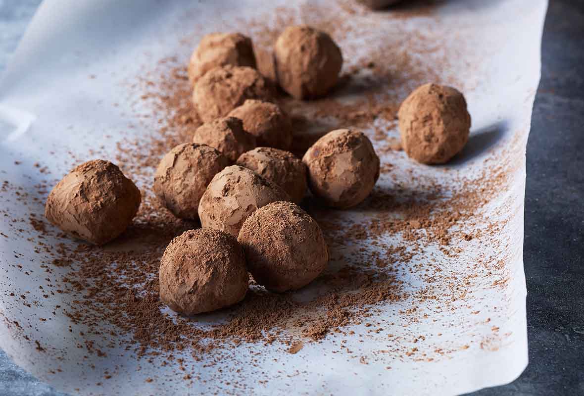 A sheet of parchment paper topped with chocolate truffles and a sifter of cocoa powder on the side