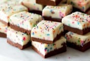 A stack of squares of birthday cake fudge on a white marble platter.