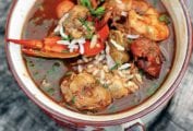 A two-handle bowl of seafood gumbo on a piece of wood.