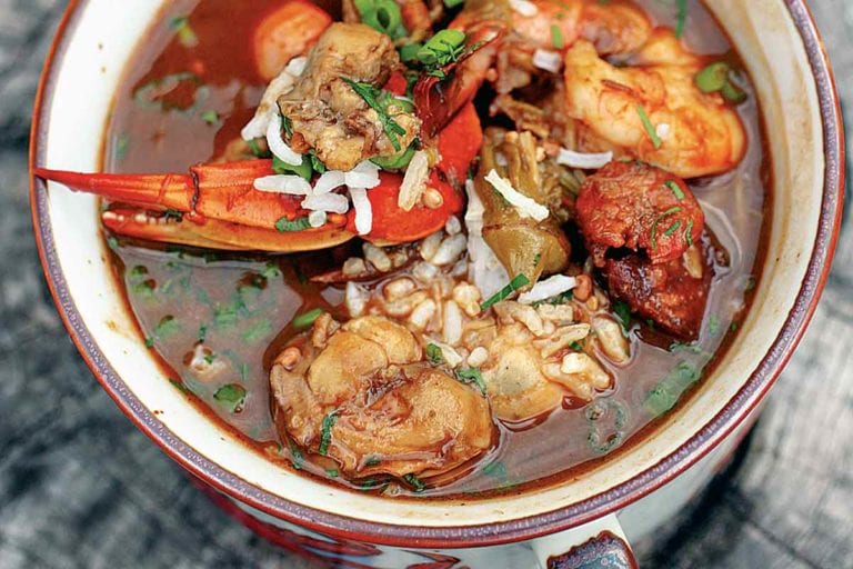 A two-handle bowl of seafood gumbo on a piece of wood.