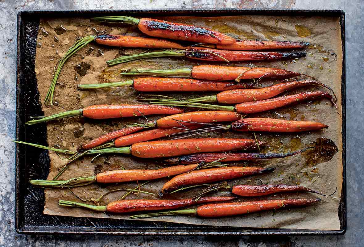 A bunch of roasted sweet and spicy carrots on a parchment-lined baking sheet.