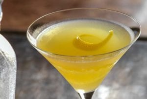 Martini glass filled with yellow Bee's Knees cocktail--honey, gin, and lemon--with a lemon twist
