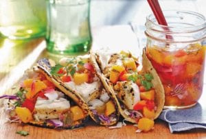 An open jar of peach salsa next to three fish tacos topped with peach salsa.