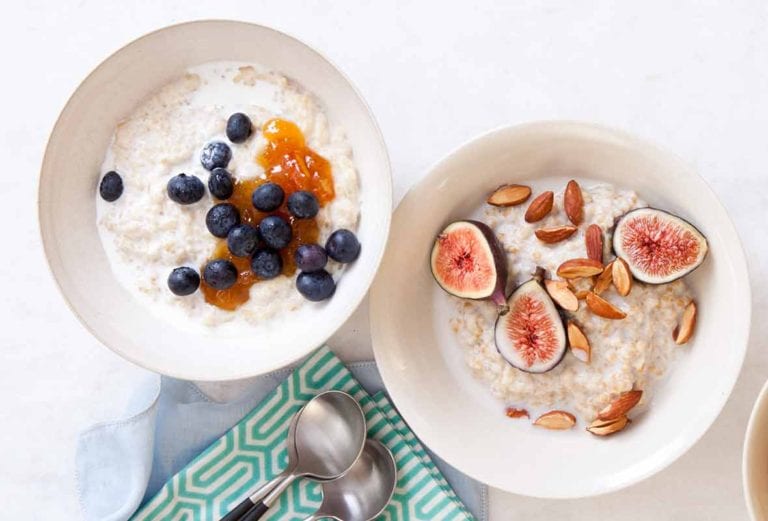 Two white bowls filled with porridge; one topped with blueberries and the other with figs and almonds