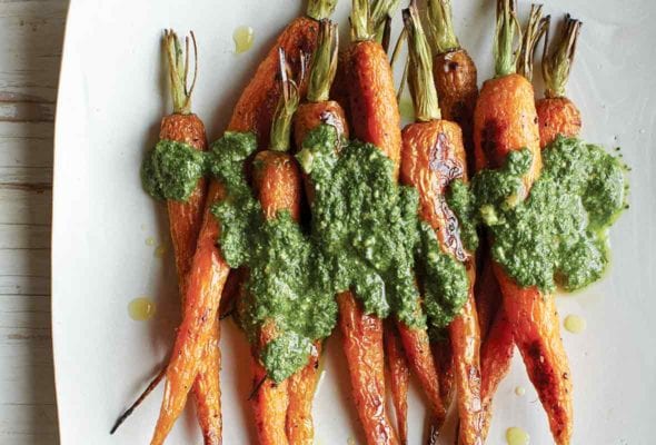 A white platter with nine roasted carrots covered in carrot top pesto.