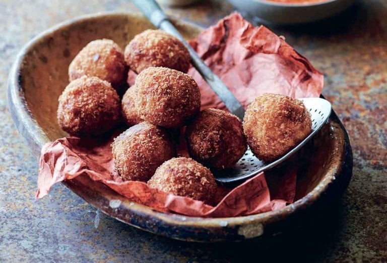 A large bowl filled with fried arancini balls and a small bowl of red pepper sauce on the side