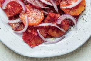 A white plate filled with blood orange and red onion salad with a grinding of pepper on top.