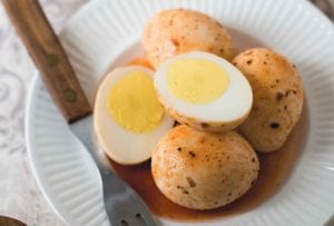 A white plate topped with four Cajun pickled eggs, one of which is cut in half. A fork rests on the plate.
