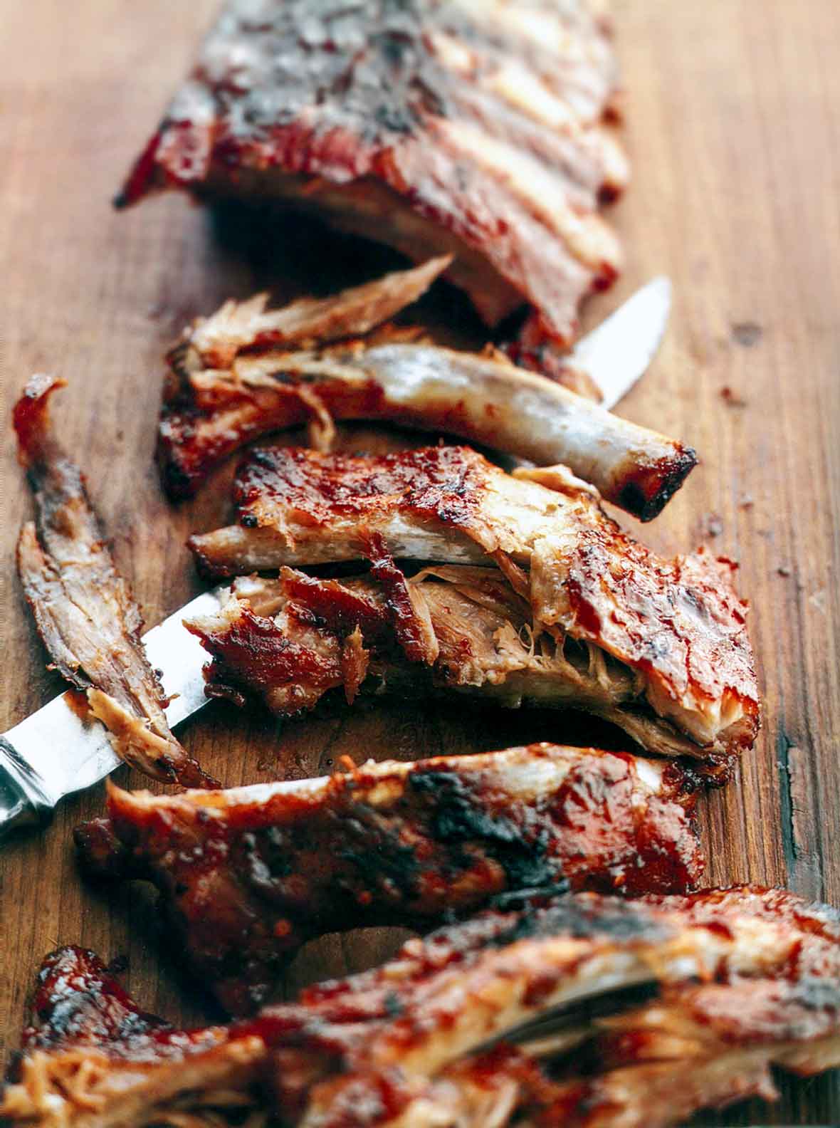 A slab of fall-off-the-bone baby back ribs with a knife cutting them into individual ribs.