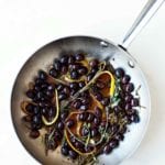 A skillet filled with black olives in an infusion of herbs and lemon and orange peel