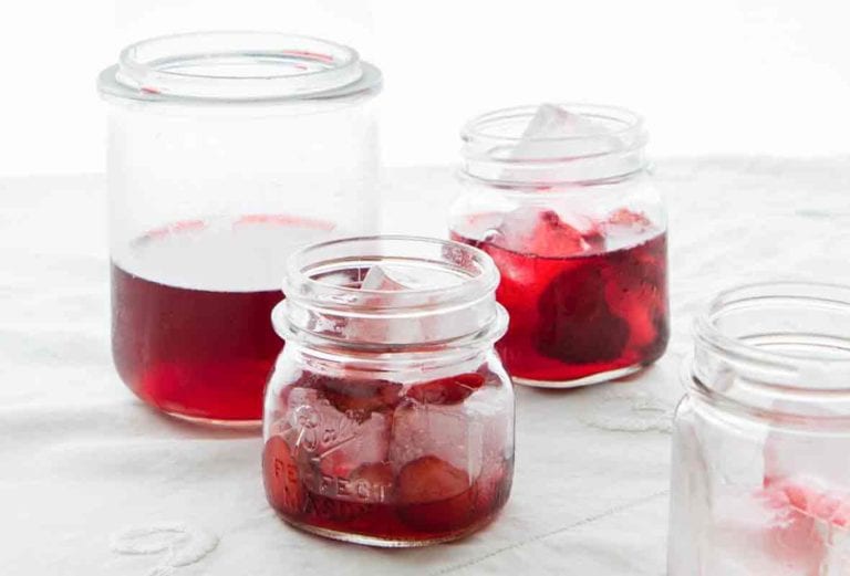 A tall bottle and several small jars filled with strawberry punch and ice cubes.