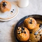 A metal baking dish with two baked apples in it, each apple topped with almonds and currants