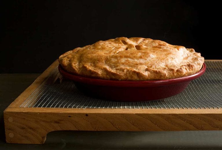 An apple pie with Cheddar crust in a red pie pan on a cooking rack