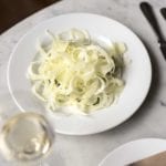 White plate of shaved fennel salad with provolone cheese, and a glass of wine