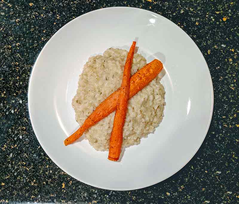 Plate of lemon-thyme risotto with two seared carrots on top all on a marble counter