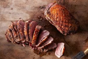 Two seared duck breasts, one sliced, the other whole on a wood cutting board
