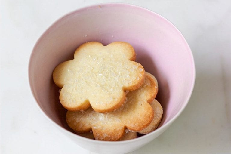 A pink bowl filled with flower-shaped sugar cookies topped with decorating sugar