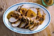 Braised pork loin with rosemary topped with a mustard-garlic sauce on a white plate on wood