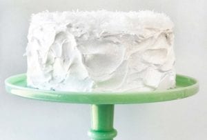 A white coconut layer cake, with 7-minute frosting topped with shredded coconut on a green cake stand