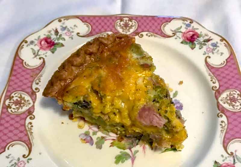 A slice of Broccoli-Cheddar quiche on a flowered plate