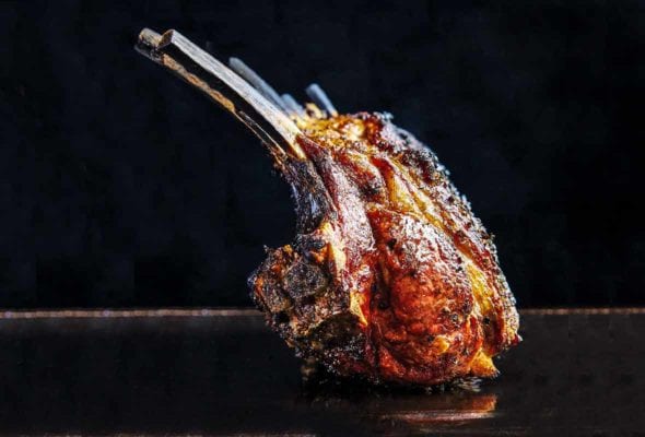 A deeply browned grilled rack on lamb sitting on a black surface