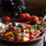 Wood bowl of panzanella from Ina Garten with bread chunks, tomatoes, peppers, cucumbers, basil, and parsley