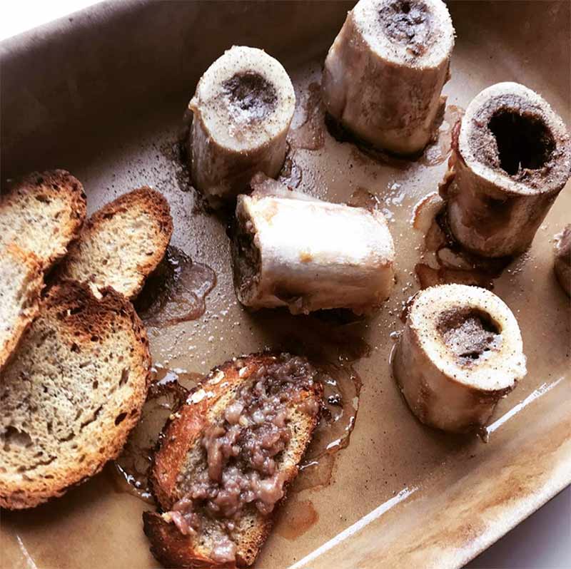 A tray with five shanks of roasted bone marrow and slices of toasted bread spread with the marrow