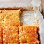 A parchment-lined square pan of buttermilk cornbread cut into squares, with one square missing.