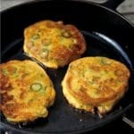 Three okra cornmeal cakes--with rings of green okra in it--in a black cast iron skillet