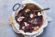 A pan lined with parchment paper containing sliced roasted beets, chunks of feta cheese, a dressing, and a spoon