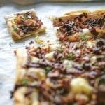 A sheet pan with an onion thyme tart on it, covered with cooked onions, thyme on a puff pastry crust