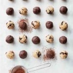 25 chocolate energy balls, made with dates, almond butter, almonds, and cacao powder, on white marble