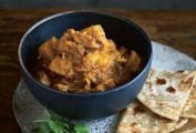 A bowl of devil's curry--chunks of chicken thighs, potatoes, and curry paste with naan bread on the side