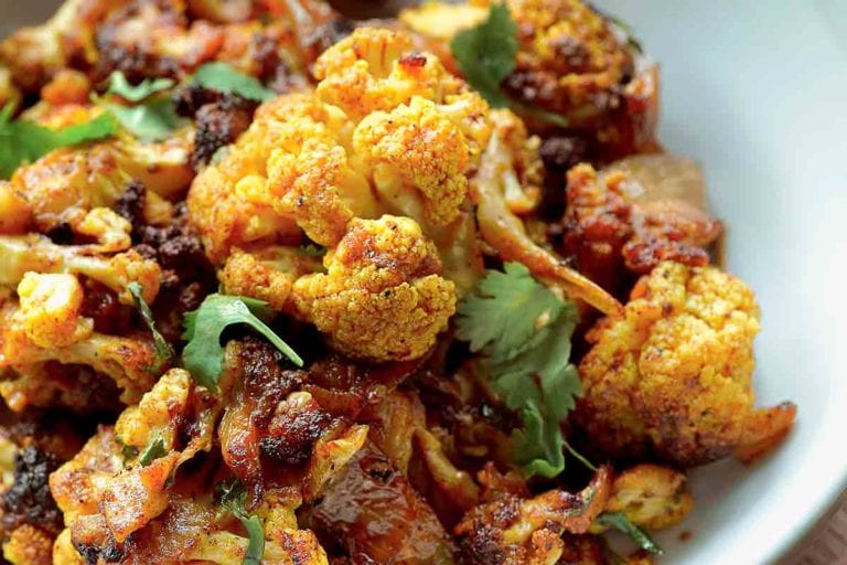 A bowl of roasted curried cauliflower mixed with onions and topped with cilantro