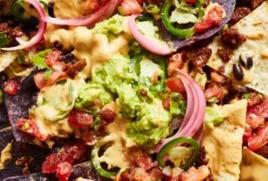 A close up of vegan nachos made with seitan, plus a sour lime cream, cashew, pickled red onions, avocado, jalapeño, and cilantro