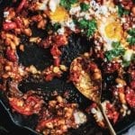 Cast iron skillet with white bean shakshuka--whit beans, tomatoes, feta cheese, eggs, and parsley