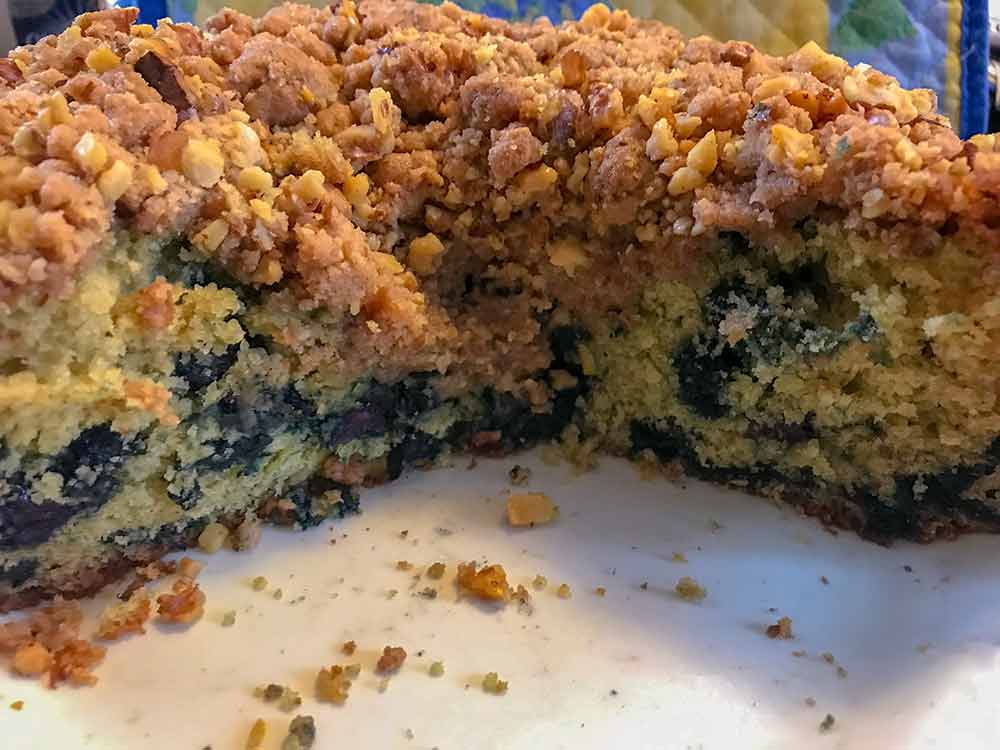 A blueberry buckle sliced into revealing the cake, blueberry layer, and sugar-nut crumb topping
