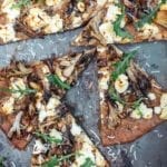 A mushroom and goat cheese pizza topped with dandelion leaves cut into six slices