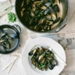 A pail and a white bowl filled with red curry mussels, as well as a bowl of discarded mussel shells